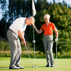 Man putting on golf green woman holding flag