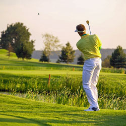 male golfer hitting ball over water on golf course